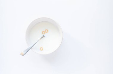 Bowl of milk with three cheerios cereal on white background. clipart