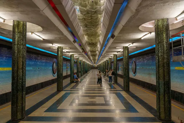 Mavi ve beyaz döşemesi olan uzun, boş bir metro istasyonu.