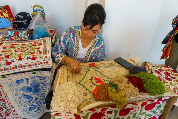 Bir kadın çeşitli renkli ipliklerle dolu bir masada oturuyor.