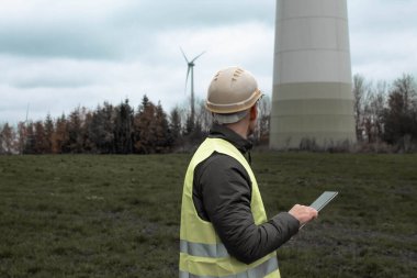 Genç mühendis sahada yel değirmenleriyle tablet kullanıyor.