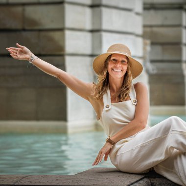 Genç kadın gülümsüyor ve neşe içinde su kenarında poz veriyor.