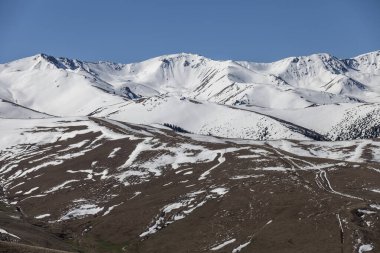 Karla kaplı dağlar ve mavi gökyüzünün altında kısmen erimiş arazi.