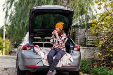 Sarı bereli kadın bagajında kahveyle oturuyor.