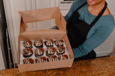 A dozen chocolate cupcakes in box held up by baker clipart