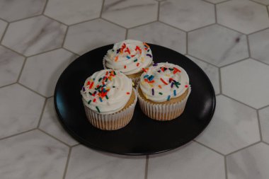 Trio of vanilla cupcake with rainbow sprinkles sitting on plate clipart