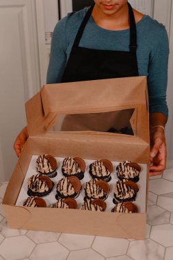 Female baker boxing a dozen chocolate and peanut butter cupcakes clipart