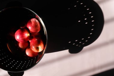 Red Apples in Colander and Dramatic Shadows on Lilac Backdrop clipart