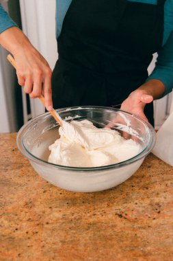 Baker in kitchen mixing vanilla frosting in bowl clipart