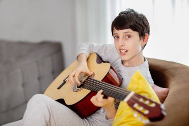 Rahat bir evde kanepede uzanmış gitar çalan bir çocuk.