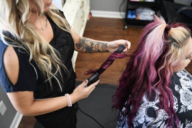 Stylist curling client's vibrant pink hair in a modern salon set clipart