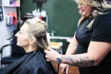 Yeşil gruplu bir kuaförde müşterinin saçı üzerinde çalışan stilist