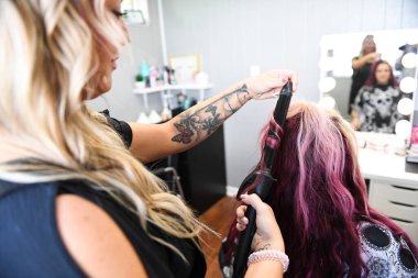 Profesyonel bir dokunuşla stilist kıvırma müşterisinin pembe saçlarını