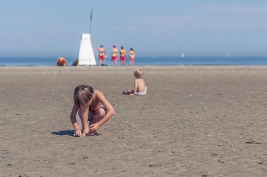 Meraklı Çocuk güneşli bir plaj gününün tadını çıkarırken deniz kabukları topluyor