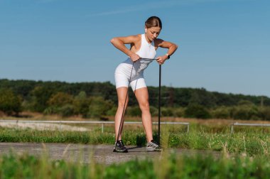 Athletic girl in sportswear doing exercises with fitness rubber clipart