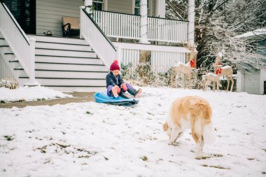 Child sledding near a snowy porch and festive decorations clipart