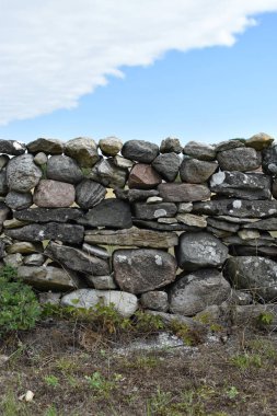Yeşil bitkiler ve parlak bulutlar arasında sağlam bir taş duvar yükseliyor.