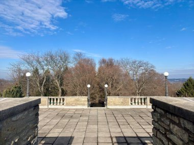 Kaliteli lambalar, ağaçlar ve parlak mavi gökyüzü olan açık taş teras.