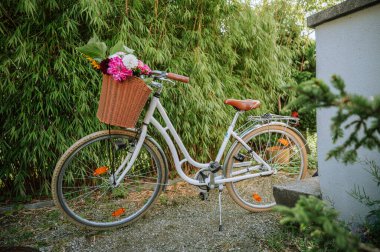 Açık havada yeşilliğin yanında bir sepet çiçekli beyaz bisiklet.