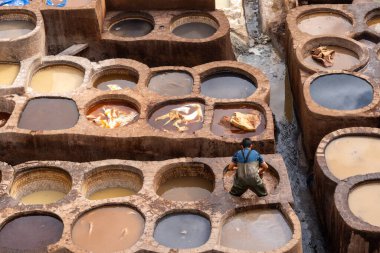 Mavi bluzlu işçi ve Fez tabakhanesinde, etrafı boya çukurlarıyla çevrili.