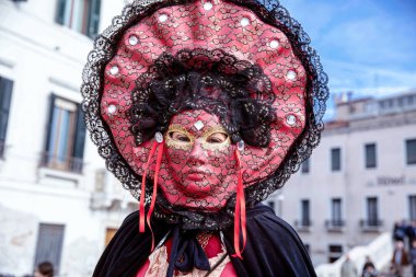 Açık havada kırmızı dantel kostümlü Venedik maskeli figürü.