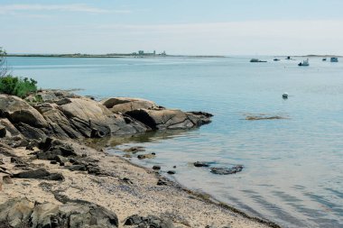 Uzakta kayalık kıyı şeridi, okyanus ve tekneleri olan Maine Sahili.