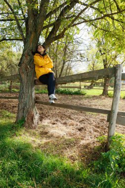 Sarı ceketli ormandaki bir çitin üzerinde, doğayla çevrili.