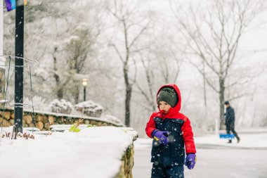 Child in red coat playing outdoors with an adult in the background clipart