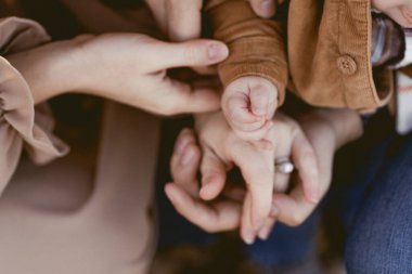 Close-up of baby hand resting on parents' hands clipart