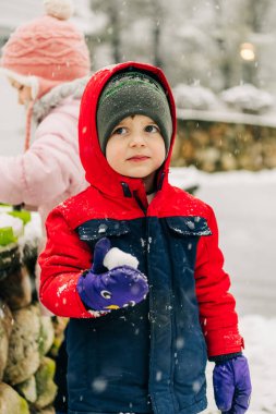 Kırmızılı çocuk arka planda başka bir çocukla kartopu tutuyor.