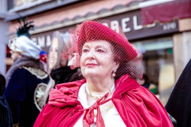 Şenlikte peçeli, kırmızı elbiseli, zarif, olgun, beyaz bir kadın.