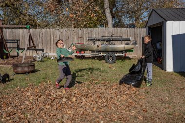 Güneşli bir günde arka bahçede yapraklarla oynayan iki çocuk.