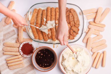 Children placing coffee-soaked savoiardi biscuits on cream clipart