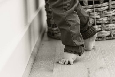 Barefoot toddler standing on wooden floor near a wicker basket clipart