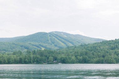 Huzurlu dağ manzarası, kayak yokuşları ve önünde sakin bir göl..