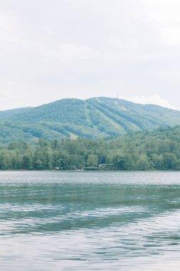 Huzurlu dağ manzarası, kayak yokuşları ve önünde sakin bir göl..