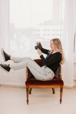 Kadın pencerenin yanındaki kırmızı sandalyede kamerayla şakacı poz veriyor.