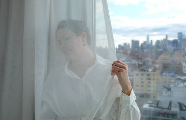 Kadın perdeyi arkaplanda gökdelen ile tutuyor.