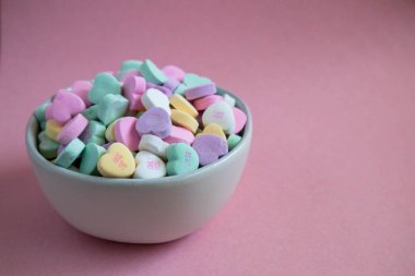 Sohbet pembe arka planda beyaz kasede renkli şeker kalpler.