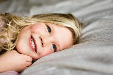 Yatakta uzanmış gülümseyen sarışın bir kızın yakın çekimi.