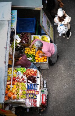 Sokak tezgahından meyve toplayan kadınlar yukarıdan izleniyor.