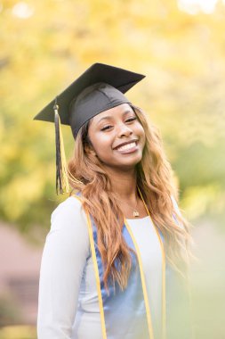 Mezuniyet şapkalı siyahi kadın, arka planda sonbahar kurşunları.