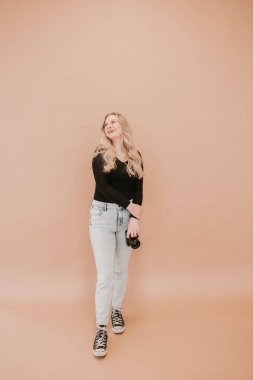 Gülümseyen fotoğrafçı bej bir arkaplanda kamera tutuyor.