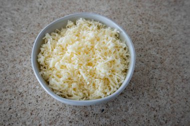 Ceramic white bowl full of shredded white cheese, speckled countertop. clipart