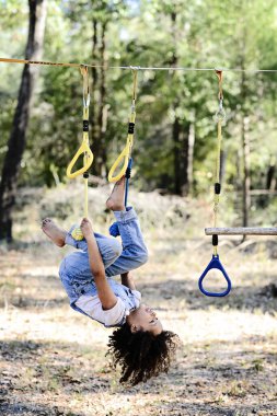 Tulumlu bir çocuk sarı oyun alanının iplerinde baş aşağı asılı duruyor.