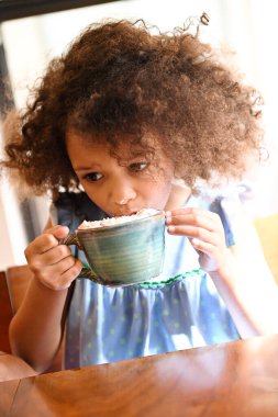 Bardaktan kremayla sıcak çikolata yudumlayan genç bir kız..