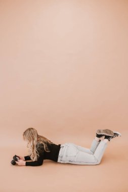 Woman lying down reviewing camera settings on a beige background clipart