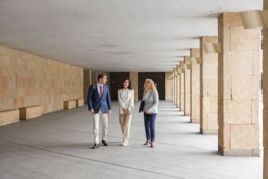 Modern bir bina koridorunda yürüyen ve konuşan iş adamları