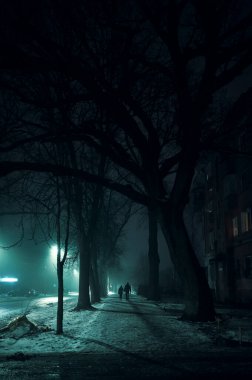 Sokaklar sisli, yol boyunca fenerler ve karşıdan karşıya geçen bir adam var.