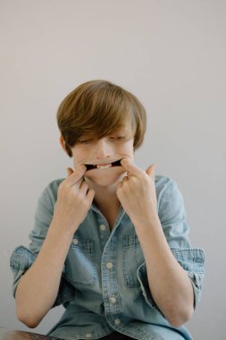 Chambray tişörtlü, neşeli suratlar yapan genç bir çocuk.