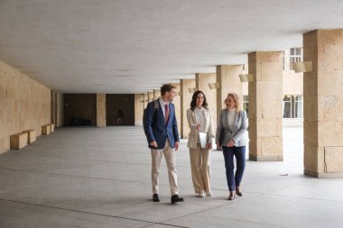 Modern bir bina koridorunda yürüyen ve konuşan iş adamları